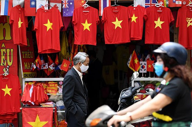 Người dân đeo khẩu trang đi qua một cửa hàng bán đồ lưu niệm tại Hà Nội, sau khi quy định giãn cách xã hội được nới lỏng. (Ảnh: AFP)